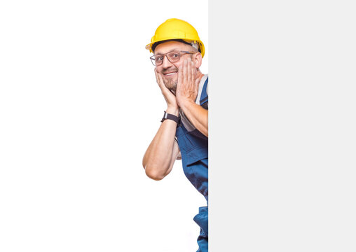 Ecstatic construction worker holding white board, isolated on white background. Handsome repairman showing blank empty paper billboard with blank space for text. Craftsman against white wall