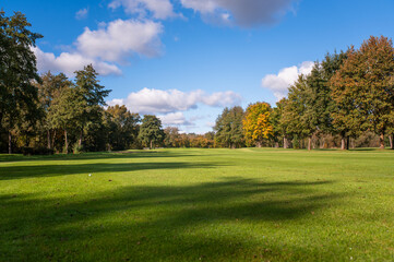 Golf fairway surrounded by autumn trees under blue sky
