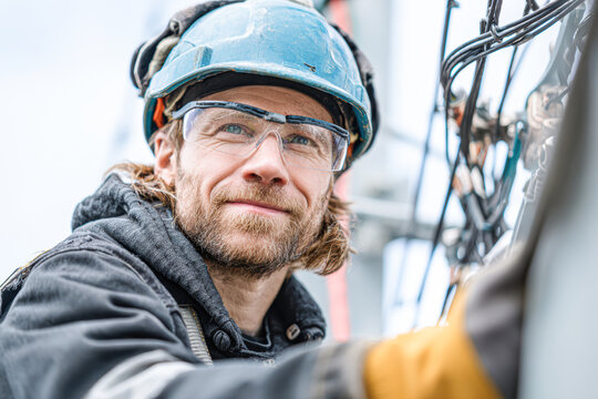 A focused worker in safety gear, smiling while working on equipment, showcasing dedication and professionalism in a technical environment. - Powered by Adobe