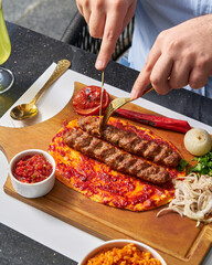Adana kebab on flatbread with tomato and pepper on a wooden board with side dishes
