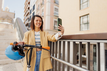 An Asian woman is riding an electric scooter while using her pho
