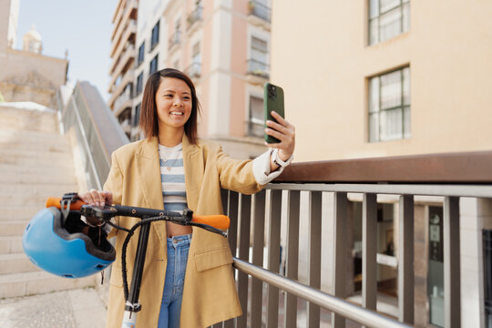 An Asian woman is riding an electric scooter while using her pho

