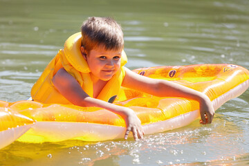 Little boy swimming in the lake on a warm summer day. The child enjoys water procedures, he refreshes himself with cool water
