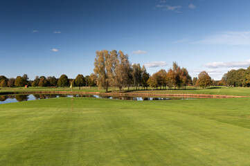 Golf green with flag and pond surrounded by autumn trees