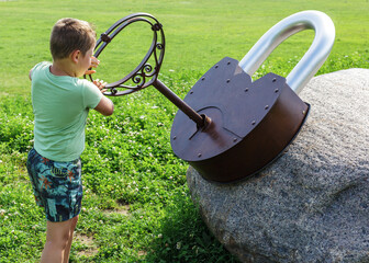 A little boy playing in the park and trying to unlock a huge lock