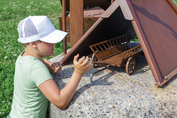 A little boy plays with a metal antique carriage model on a stone during a walk