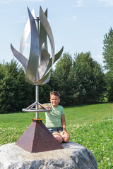 A little boy sits on a stone next to the wind sculpture and looks at us