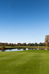 Obraz premium Golf green with flag and pond surrounded by autumn trees