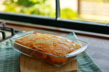 Peach cake in a glass dish on a wooden board on the kitchen counter
