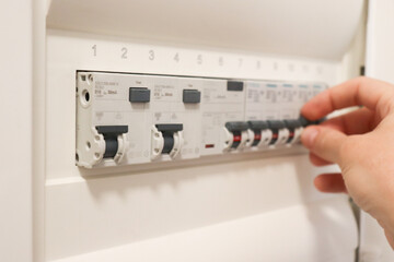 Electrician hand switching circuit breakers in modern electrical panel. Safety and maintenance concept in industrial power distribution system.