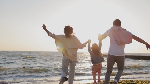 Full body back view young happy parents mom dad with little child kid daughter girl wearing casual clothes rest in free time walk run to sea sand shore beach outdoor in summer day. Family day concept