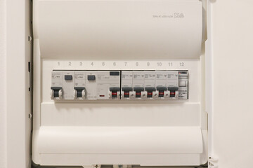 Modern electrical distribution panel with circuit breakers and switches installed on white wall. Close-up view of technology, energy control and safety system.