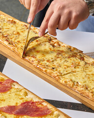 A long rectangular pizza with a knife on a wooden board in a restaurant setting