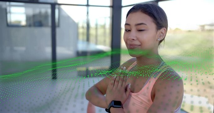 Woman breathing with palms together on patio, green particle wave guiding wellness and smile