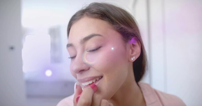 Woman bringing lipstick to lips and applying neatly for beauty, purple sparkles rising over mouth