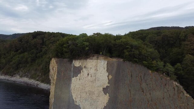 Drone footage flying backward from Kiseleva Rock cliff with man standing among trees on top