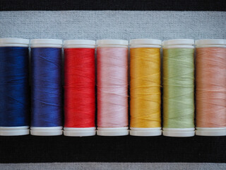 Colorful spools of sewing thread neatly arranged on black and white striped fabric background