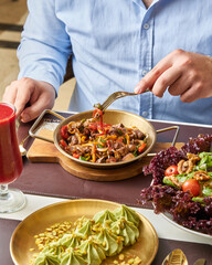 Man eating stir fry with vegetables and meat at a restaurant with salad and dessert on the table