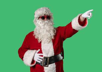 Santa Claus with a white curly beard, wearing a red suit and sunglasses, points his finger on a green background. Perfect for Christmas-themed compositions, advertising, and holiday layouts.