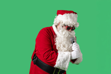 Santa Claus, with a white curly beard, wearing a red suit and sunglasses, sings songs into a microphone and dances cheerfully against a green background. Ideal for Christmas themed compositions.