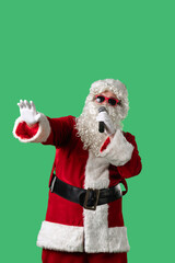 Santa Claus, with a white curly beard, wearing a red suit and sunglasses, sings songs into a microphone and dances cheerfully against a green background. Ideal for Christmas themed compositions.