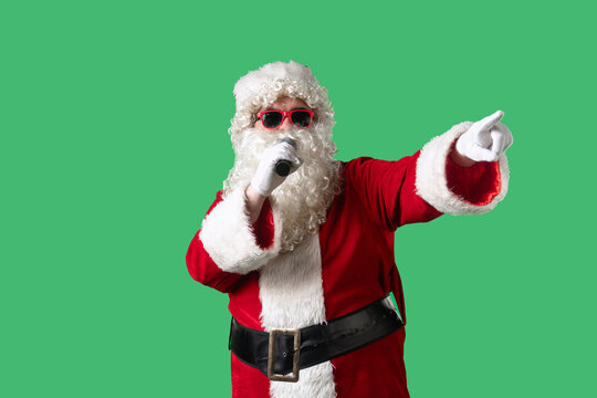Santa Claus, with a white curly beard, wearing a red suit and sunglasses, sings songs into a microphone and dances cheerfully against a green background. Ideal for Christmas themed compositions.