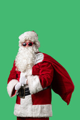 Santa Claus with a white curly beard, wearing a red suit and sunglasses, with a bag of gifts on a green background. Perfect for Christmas themed compositions, advertising, and holiday layouts.