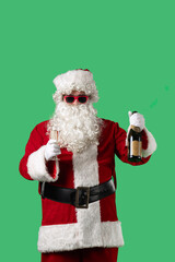 Santa Claus with a white curly beard, wearing a red suit and sunglasses, makes a congratulatory toast with a glass of champagne and a bottle in his hands against a green background.
