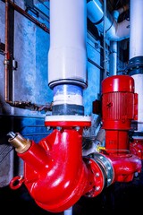 Room with water pump pipes and vertical engine painted red connected to steel and PVC pipes, with blue background light 