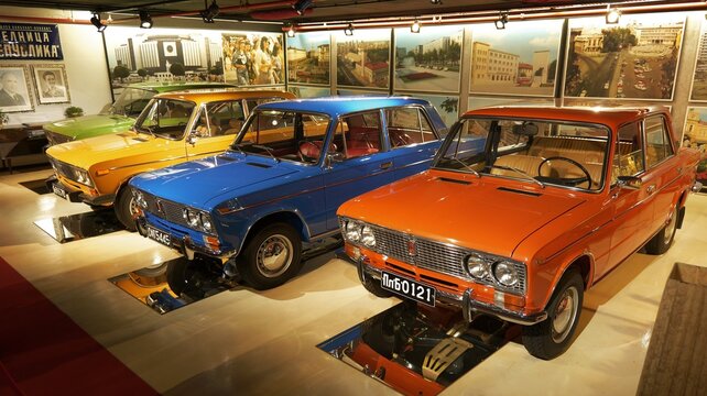 A collection of shiny Lada 2106 cars in blue, yellow, and red is photographed from a three-quarter front angle at Retro Museum Varna, illuminated to show their polished surfaces and classic Soviet des