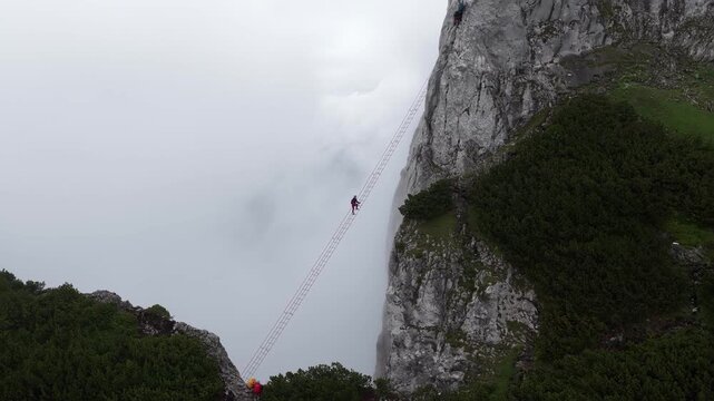 Aerial shot of a mountaineer climbing a long ladder in the foggy alps, Dachstein, Austria