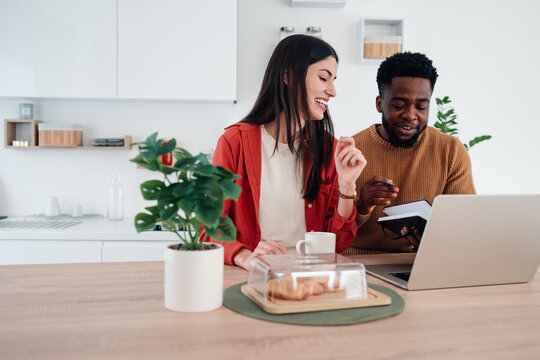 Diverse couple working together on laptop in kitchen