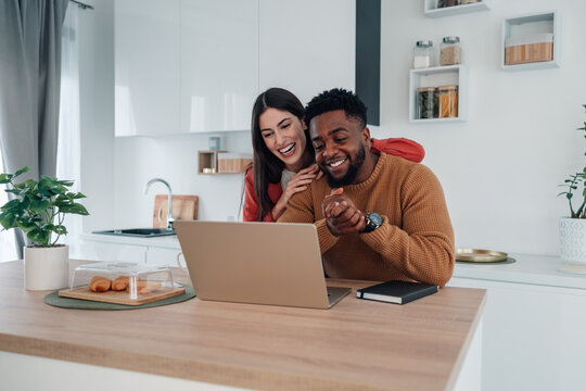 Multiracial couple laughing during video call in kitchen
