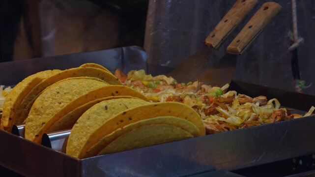 Row of Hard-Shell Tacos Standing Upright beside Cooked Chicken and Vegetables on Grill Station, Concept of Mexican Street Food and Culinary Tradition