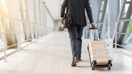 African American businessman in suit walking through airport terminal with rolling luggage. Concept of travel, business trip, mobility and global transportation