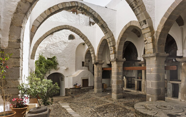 Stone courtyard, whitewashed walls and arched doorways,  cobblestone flooring, potted plants,  small tree and flowers, in the Monastery of Saint John the Theologian on the island of Patmos, Greece.