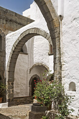 Stone courtyard, whitewashed walls and arched doorways,  cobblestone flooring, potted plants,  small tree and flowers, in the Monastery of Saint John the Theologian on the island of Patmos, Greece.
