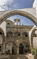 Stone courtyard, whitewashed walls and arched doorways,  cobblestone flooring, potted plants,  small tree and flowers, in the Monastery of Saint John the Theologian on the island of Patmos, Greece.