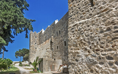 Historic stone fortress with cylindrical tower and crenellated walls surrounding the Monastery of Saint John the Theologian of Patmos, Greece.