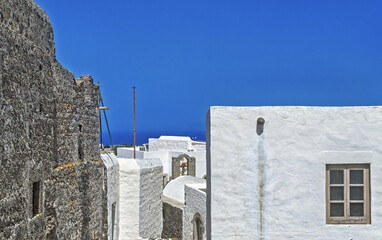 Whitewashed building with smooth stucco walls and small dark-framed windows, featuring a dome structure in Patmos, Greece. © hectorchristiaen