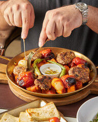 Kofta kebab with grilled vegetables in a golden pan on a wooden board