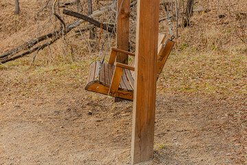 A wooden swing suspended from a sturdy post in a leaf-strewn autumn park or forest. Calm mood perfect for outdoor lifestyle, nature, or family moments in outdoor spaces.