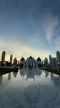 Baiturrahman Grand Mosque in Banda Aceh at sunset, featuring a beautiful garden and reflection pool in front of the mosque.