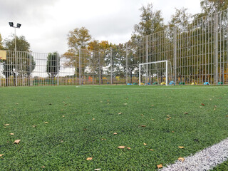 Green turf soccer field with fence and goal in autumn