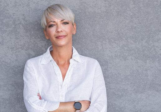 Serious adult woman standing with neutral face expression, against gray background - wall. Pretty middle age woman