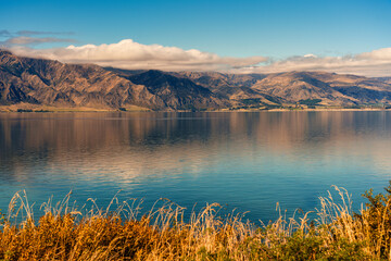 Scenic Lake Hawea with mountain range and meadow under blue sky in New Zealand