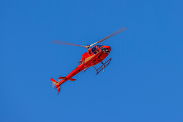 Photograph of a red helicopter in flight filming a sporting event in regional Australia