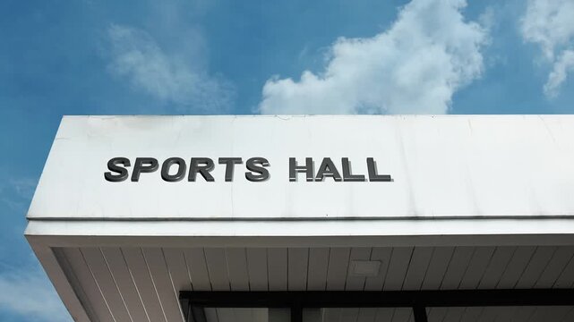 Sports Hall word sign displayed on a recreational or institutional building under a clear blue sky, symbolizing athletics, physical fitness, competition, recreation, exercise, and training