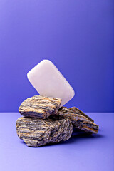 Lavender soap. Beauty and health. Minimalist composition showcases soap bar elegantly balanced on stack of textured stones, set against vibrant purple backdrop, creating harmonious aesthetic