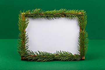 Mockup. Christmas. Blank frame adorned with fresh green pine branches, set against vibrant green backdrop, creating festive and natural atmosphere perfect for seasonal displays or invitations